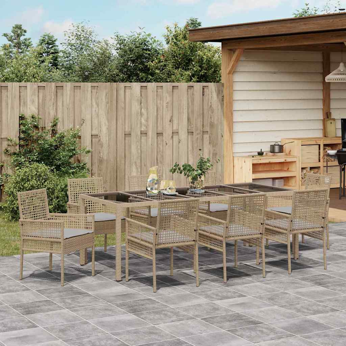 Essgruppe im Freien auf der Terrasse. Korbstühle und Tisch. Holzzaun und Schuppen im Hintergrund. Pflanzen und Geschirr auf dem Tisch.