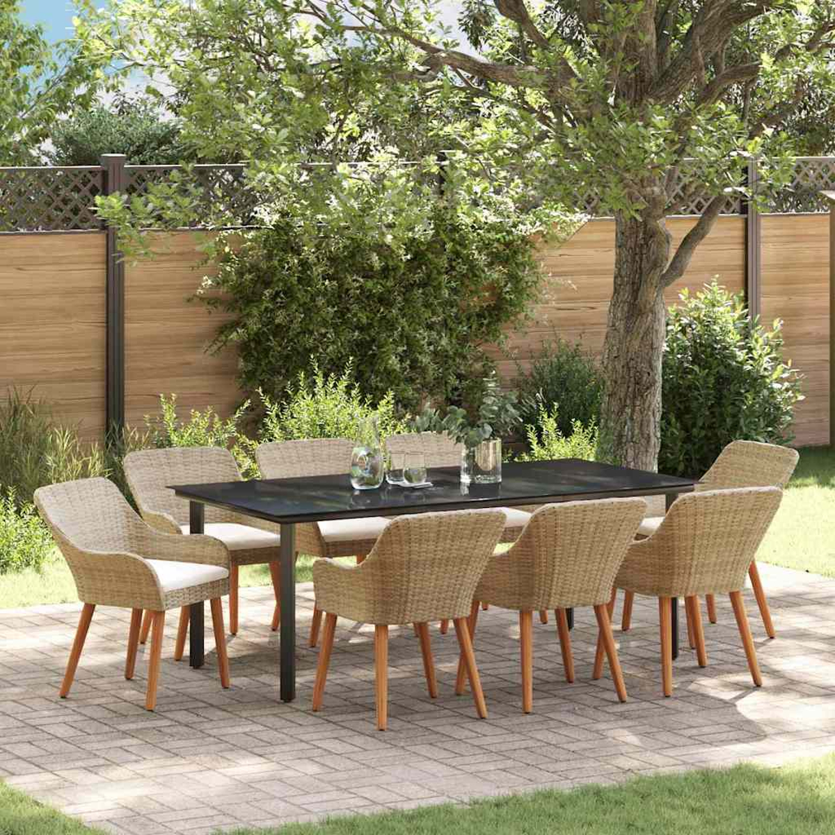 Ein Terrassenset mit einem schwarzen Tisch und Korbstühlen. Die Szene spielt in einem Garten mit Holzzaun und Bäumen im Hintergrund.