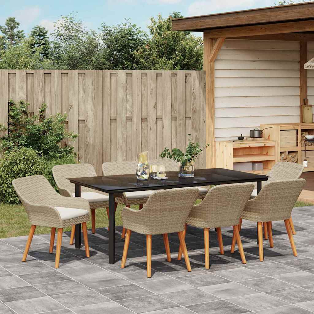 Szene im Freien. Ein Tisch mit acht Stühlen auf einer Terrasse. Ein Holzzaun und Grün im Hintergrund.