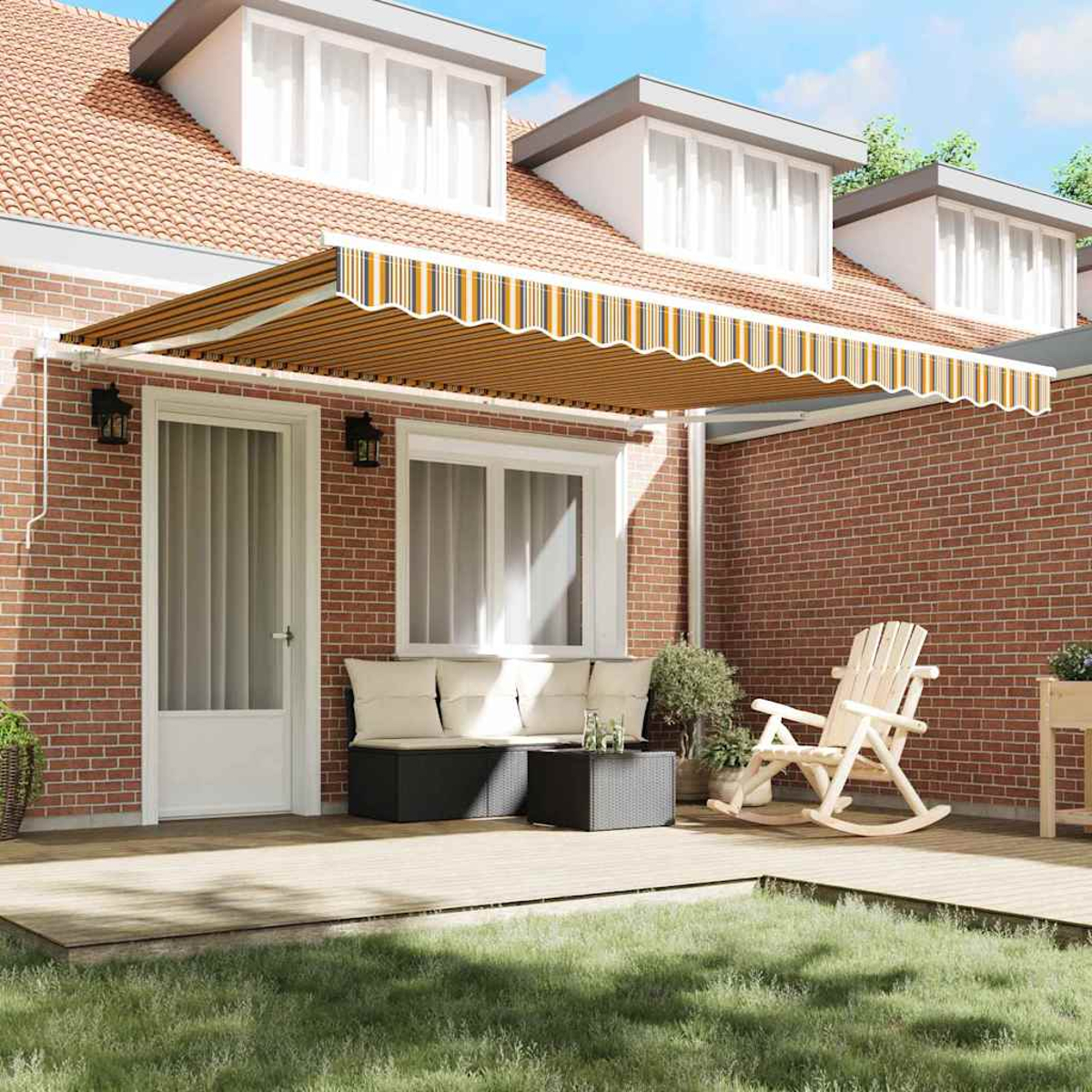 Ein Haus mit ausfahrbarer Markise, Holzterrasse mit Möbeln und Rasen im Vordergrund. Das Haus hat eine Backsteinfassade.