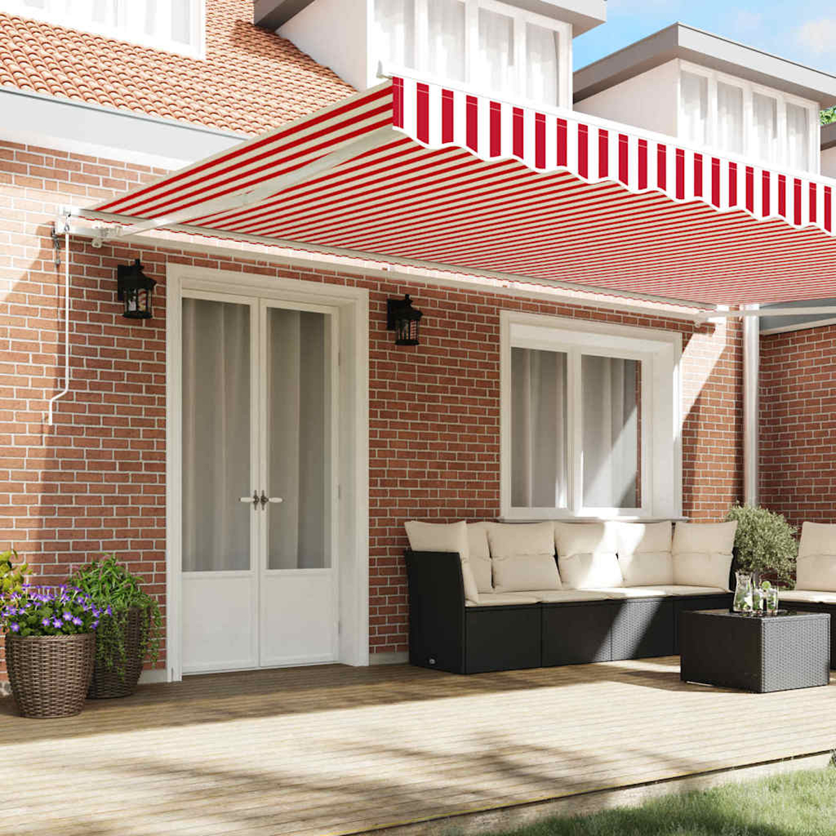 Ein Haus mit rot-weiß gestreifter Markise. Auf der Terrasse stehen ein schwarzes Sofa mit cremefarbenen Kissen, Pflanzen und ein kleiner Tisch.