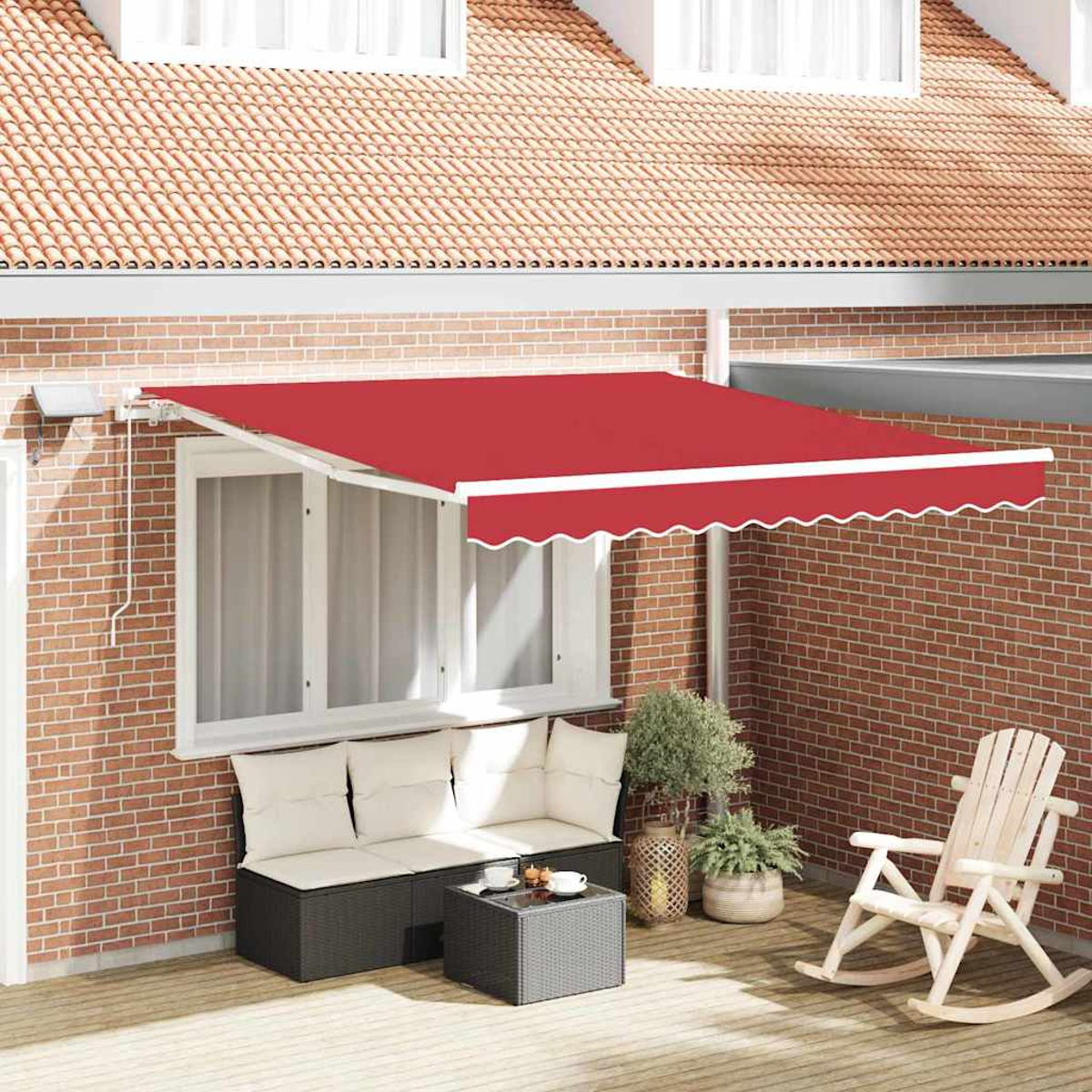 Eine rote Markise erstreckt sich über eine Terrasse mit Sofa, Tisch und Schaukelstuhl. Im Hintergrund eine Backsteinmauer und ein Ziegeldach.