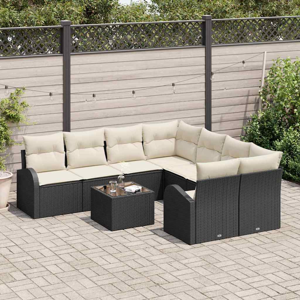 Juego de muebles de patio con estructura de mimbre negro y cojines crema. Incluye una mesa de centro y está frente a una valla de madera.