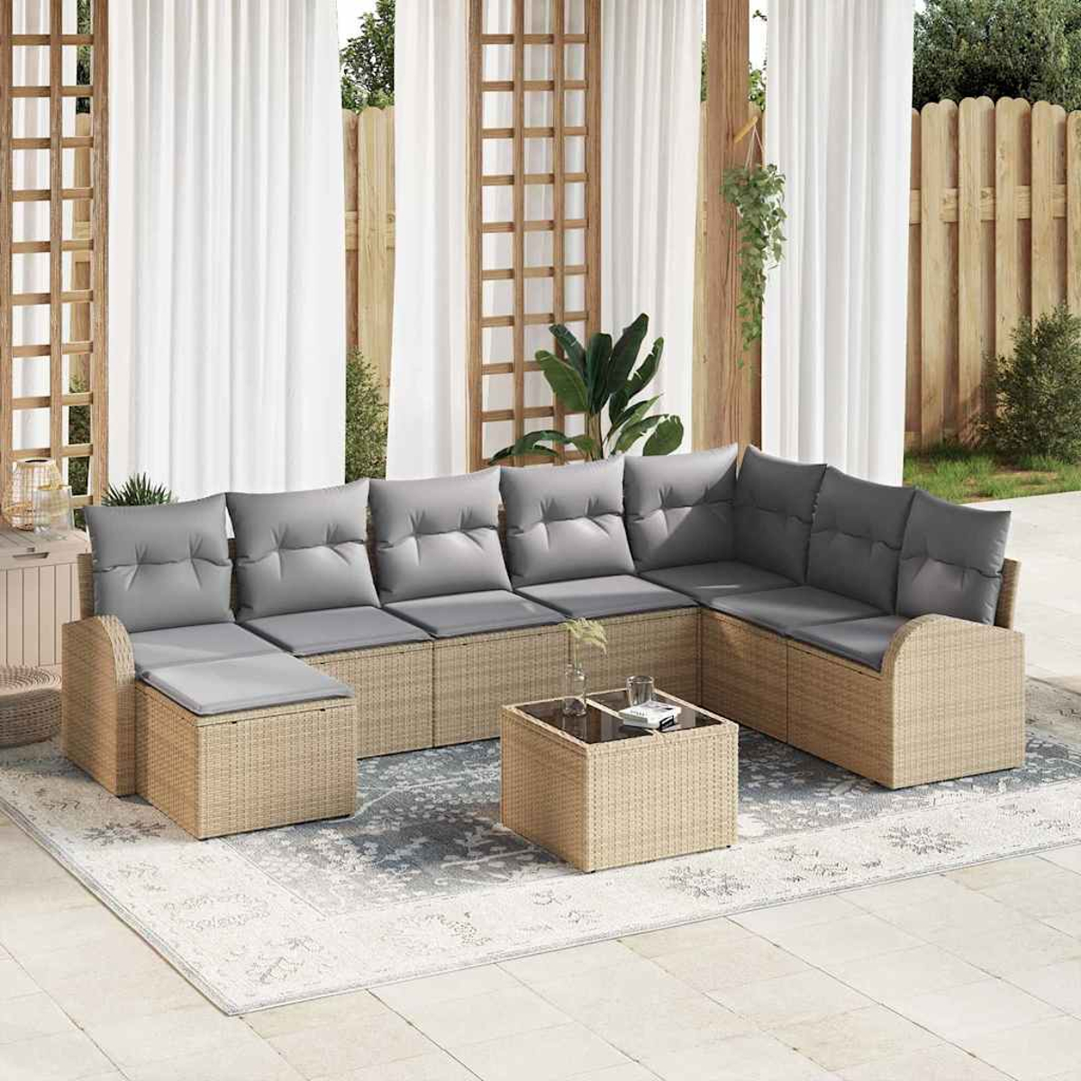 Ein Ecksofa im Freien mit grauen Kissen. Ein passender Couchtisch steht auf einem gemusterten Teppich. Weiße Vorhänge und ein Holzzaun sind im Hintergrund.