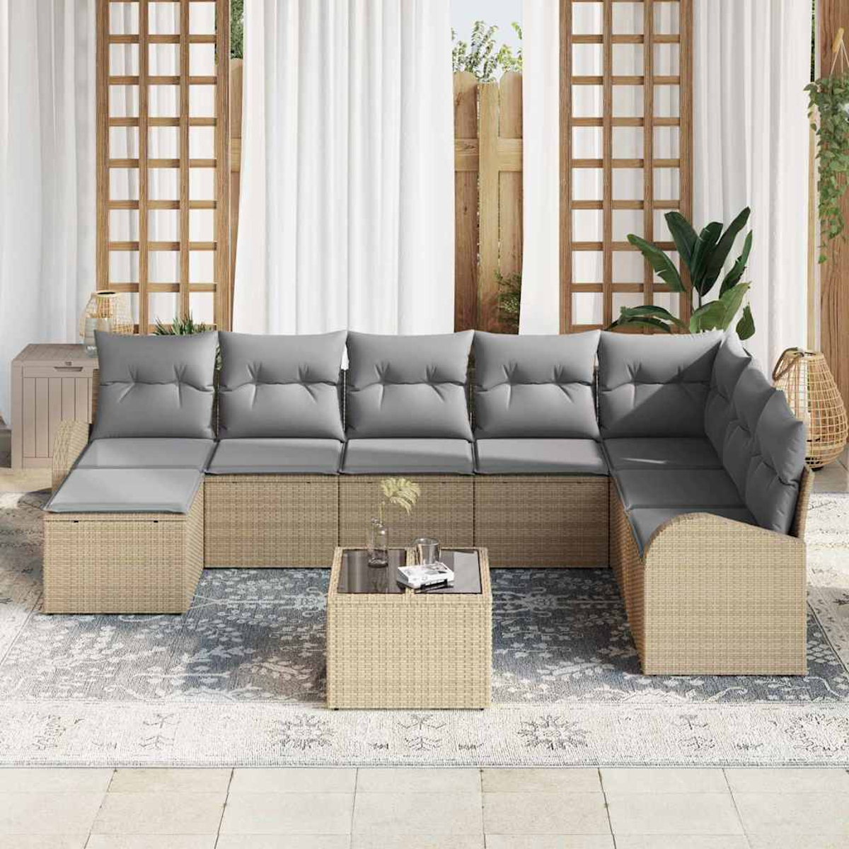 Outdoor-Ecksofa mit grauen Kissen, Korbgewebe-Gestell und Tisch mit Glasplatte auf einem gemusterten Teppich, vor einem Vorhanghintergrund.