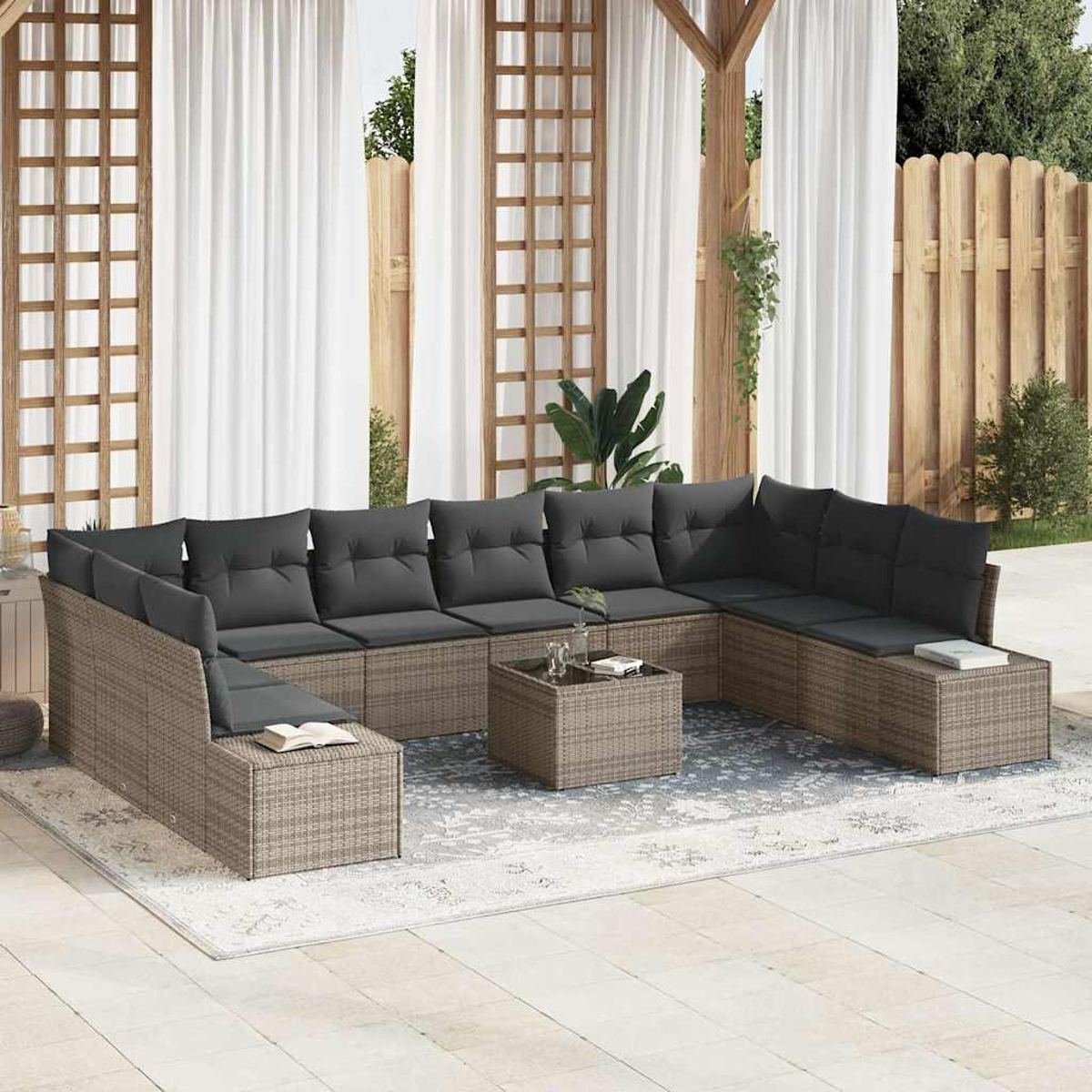 Outdoor-Ecksofa mit grauen Kissen, Couchtisch und Teppich auf einer Terrasse. Weiße Vorhänge und Holzzaun im Hintergrund.