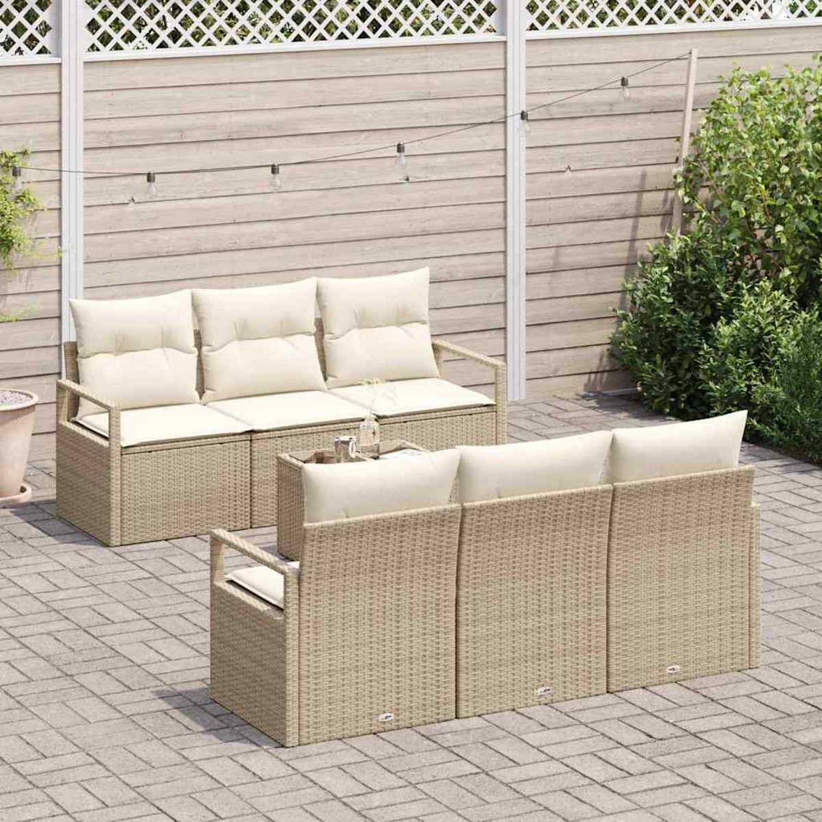 Gartenmöbel-Set aus Korbgeflecht mit cremefarbenen Kissen. Zwei Sofas stehen sich auf einer Terrasse gegenüber. Holzzaun und Grün im Hintergrund.