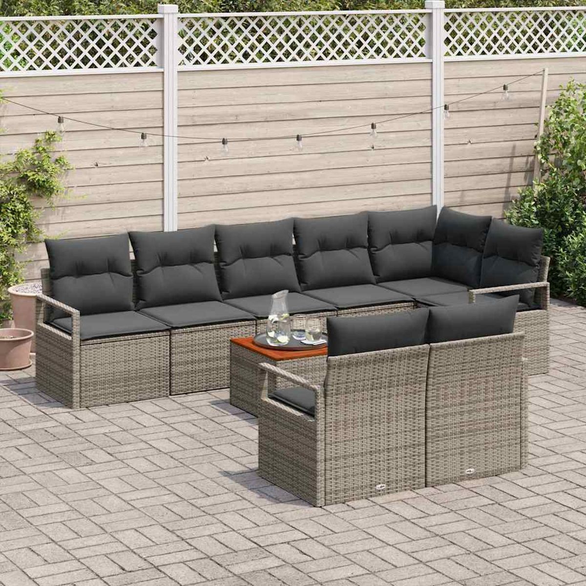 Garten-Terrassenset mit grauen Kissen. Ein kleiner Tisch mit Gläsern und einer Wasserkaraffe, alles auf einer Ziegelpflasterung mit Zaun.
