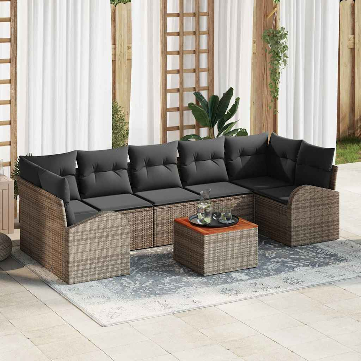 Geflochtenes Ecksofa mit grauen Kissen, Couchtisch und Teppich auf einer Terrasse. Weiße Vorhänge und Holzgitter im Hintergrund.