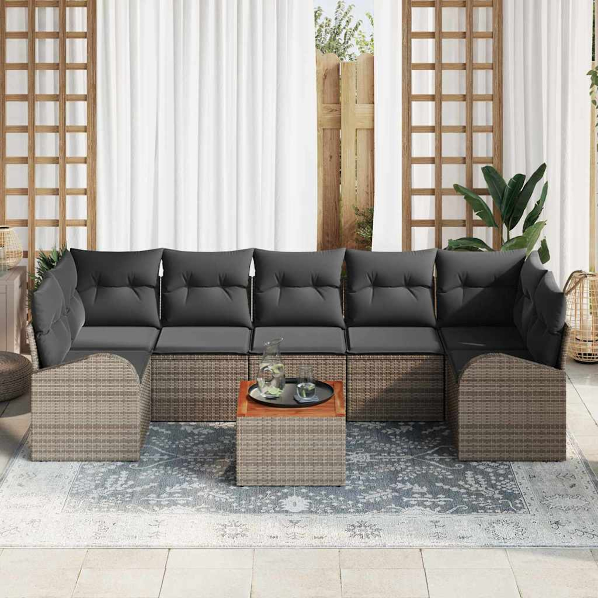 Outdoor-Ecksofa mit grauen Kissen, einem kleinen Holztisch und einem dekorativen Teppich. Weiße Vorhänge und Holzgitter im Hintergrund.