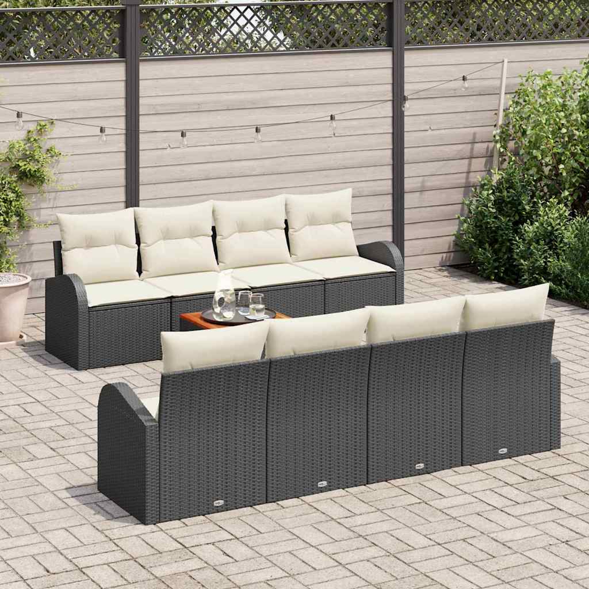 Zwei Outdoor-Korbsessel mit cremefarbenen Kissen auf einer Terrasse. Zwischen ihnen steht ein kleiner Holztisch mit Gläsern. Im Hintergrund ein Zaun.
