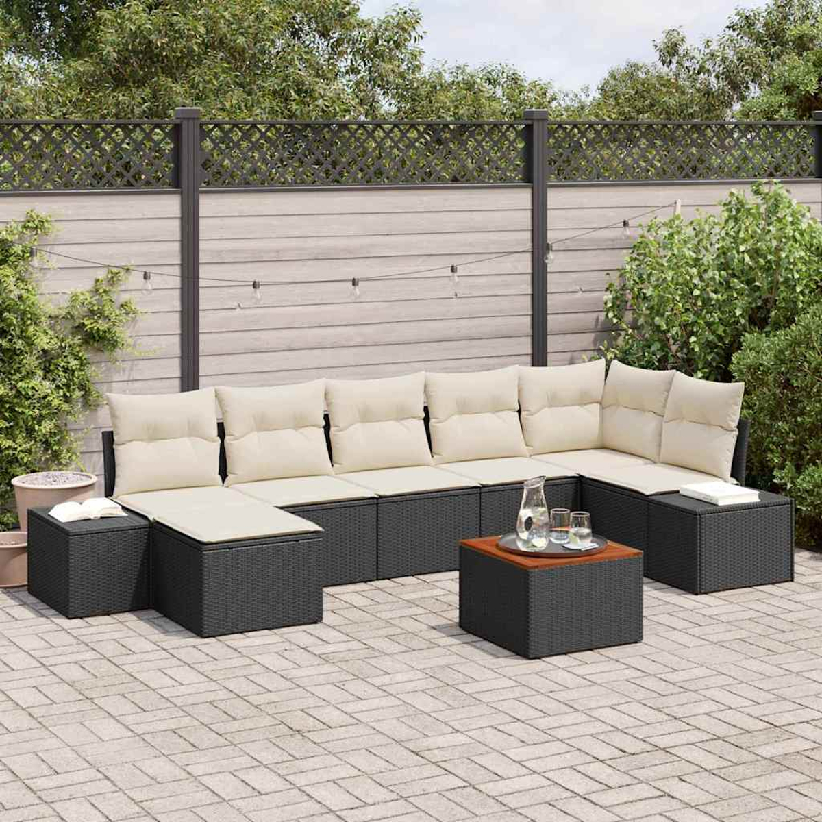 Outdoor-Ecksofa mit cremefarbenen Kissen auf einer Backsteinterrasse. Ein kleiner Tisch hält Gläser und eine Kanne. Ein Zaun und Grünzeug sind im Hintergrund.