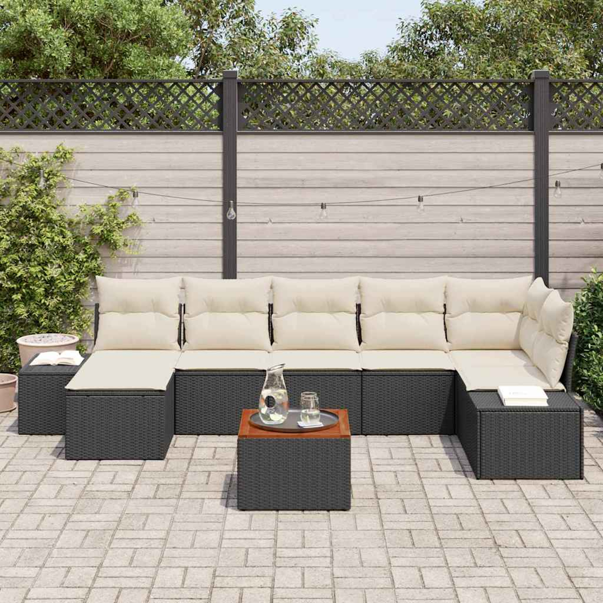 Garten-Terrassenset mit cremefarbenen Kissen, dunkelgrauem Korbgeflecht und einem Tisch mit Holzplatte. Auf dem Tisch stehen ein Glaskrug und Gläser.