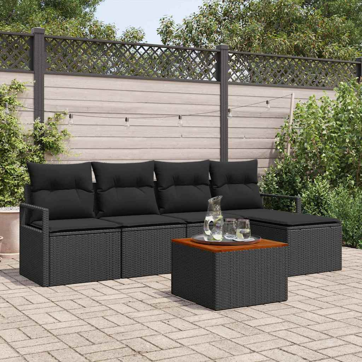Outdoor-Terrassenset mit schwarzen Kissen, einem Couchtisch mit Holzplatte und Hintergrund aus Holzzaun und Pflanzen.