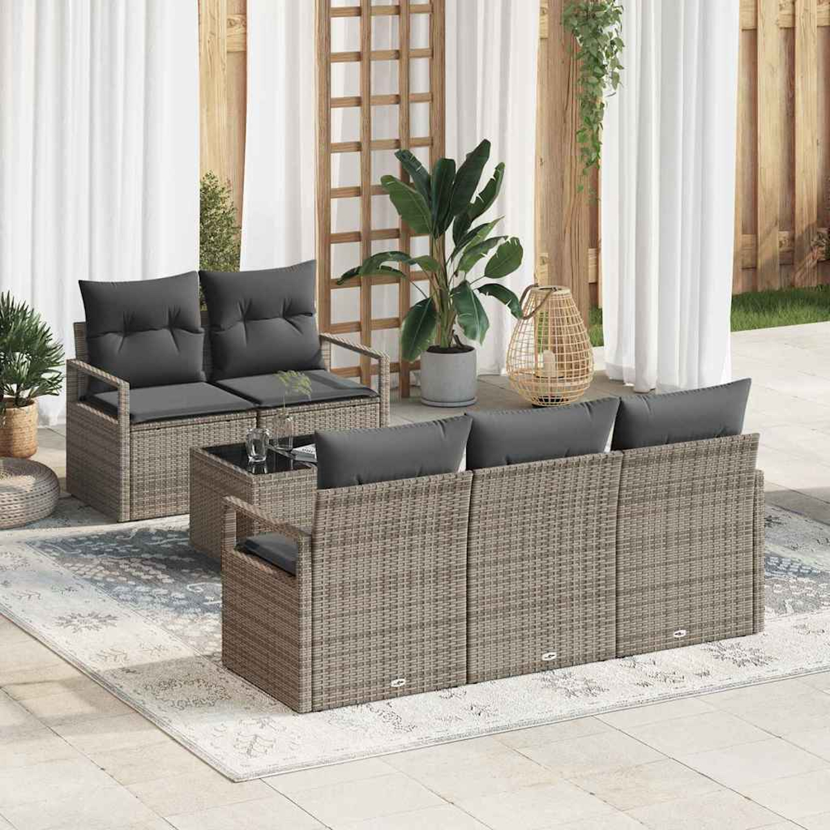 Gartenmöbel-Set mit grauen Kissen, einem Tisch mit Glasplatte und Pflanzen. Auf einem Teppich, mit Vorhängen im Hintergrund.
