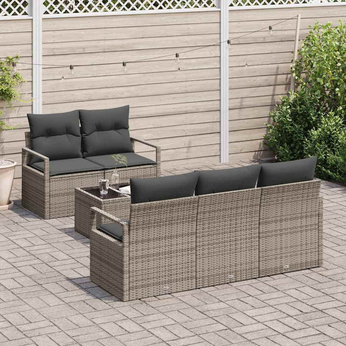 Gartenmöbel-Set aus Korbgeflecht mit grauen Kissen auf einer Steinterrasse. Enthält ein Loveseat, ein Sofa und einen kleinen Tisch. Holzzaun im Hintergrund.