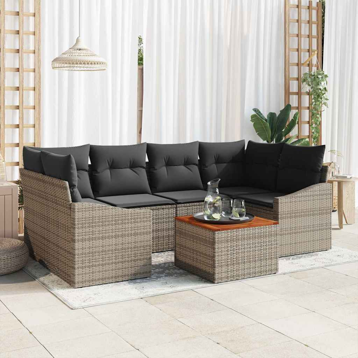 Ein geflochtenes Ecksofa mit grauen Kissen und einem Holztisch. Im Hintergrund weiße Vorhänge und eine Hängelampe.