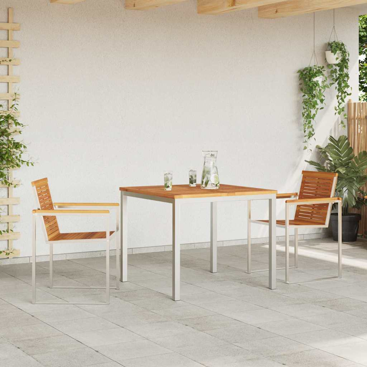 Essgruppe im Freien: Holztisch, zwei Stühle, Wasserkrug und Gläser. Pflanzen hängen und stehen auf der Terrasse.