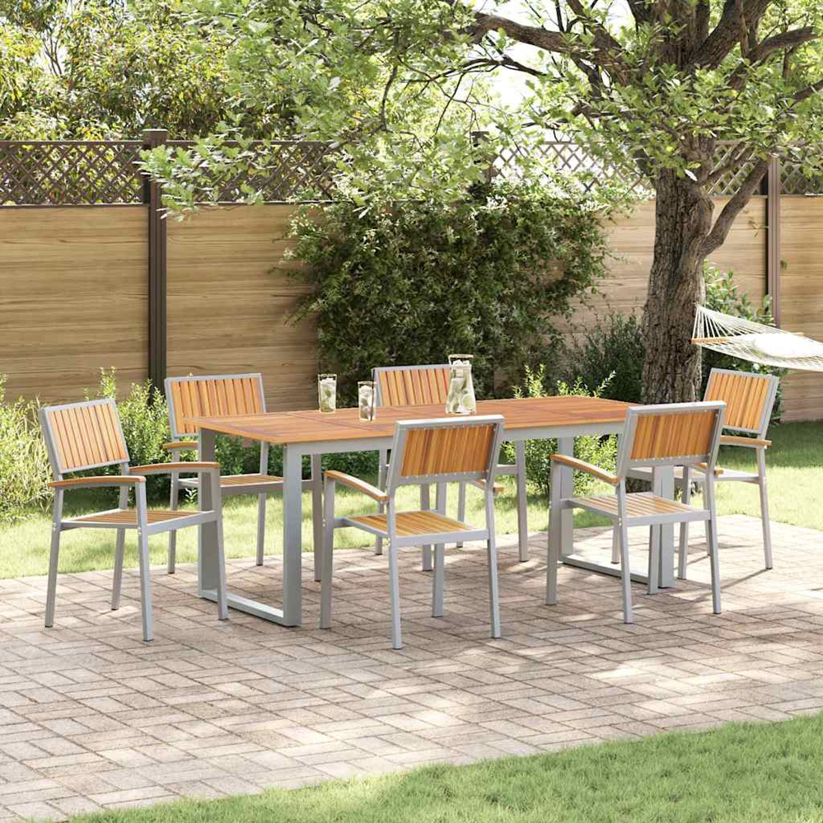 Essgruppe im Freien: Holztisch mit sechs Stühlen auf einer Ziegelterrasse, Bäume und eine Hängematte im Hintergrund.