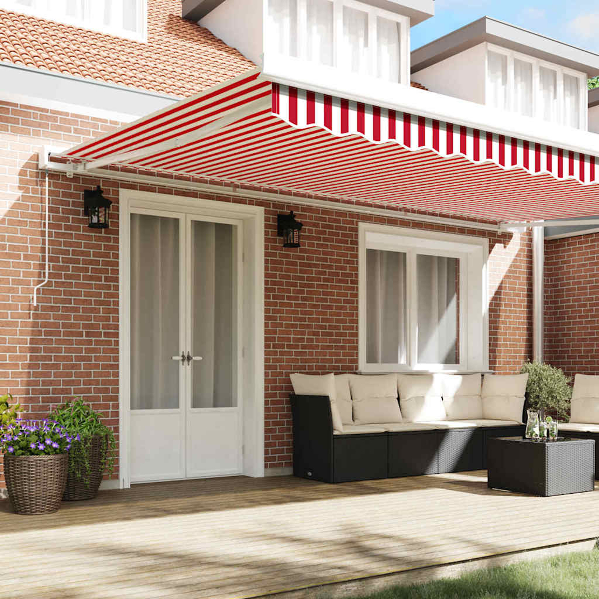 Ein Haus mit rot-weiß gestreifter Markise. Es gibt eine Holzterrasse, eine Ziegelmauer, eine weiße Tür und Gartenmöbel.