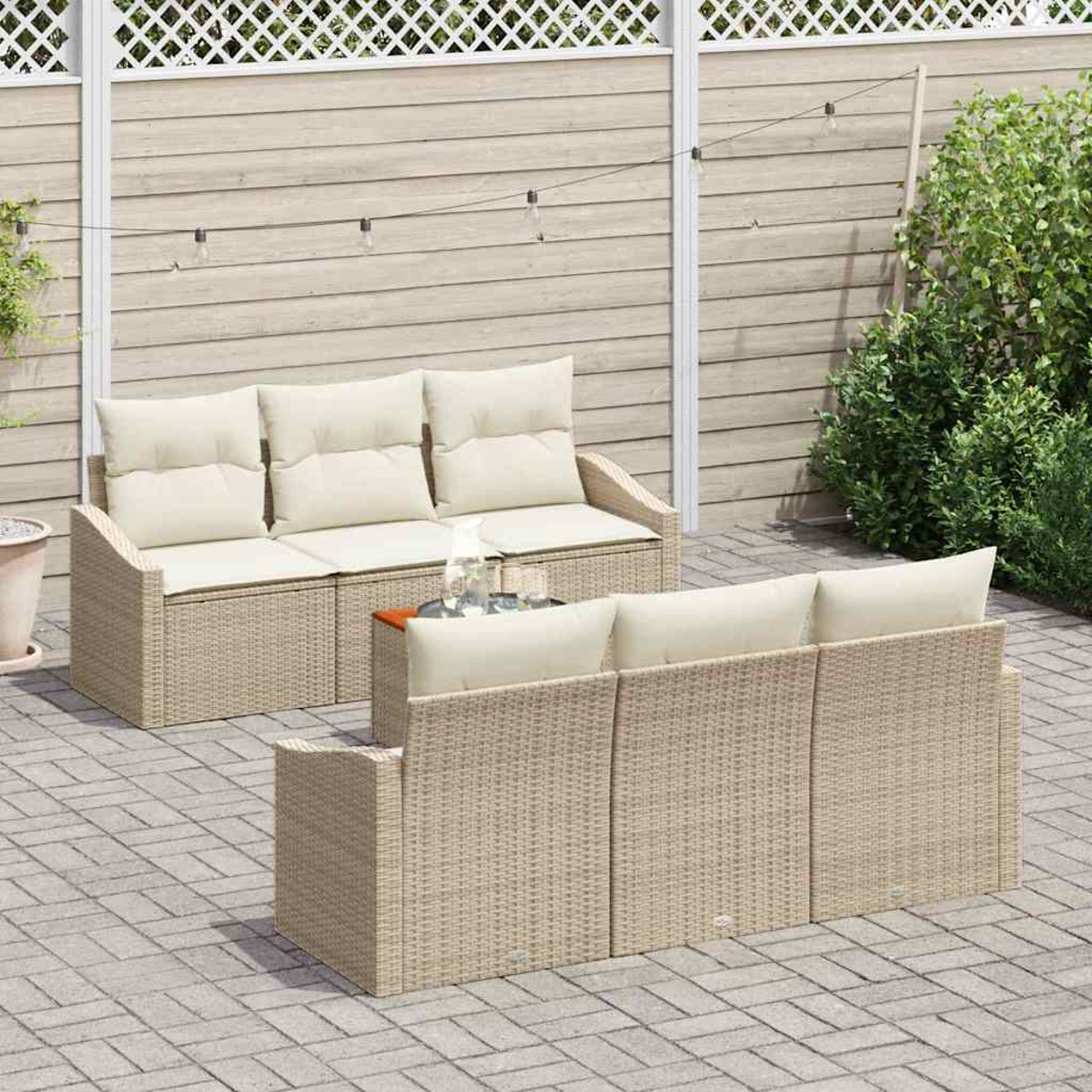 Terrassenmöbel-Set mit zwei beigefarbenen Korbsesseln und cremefarbenen Kissen. Hintergrund: Holzzaun, Pflanzen und Lichterketten.