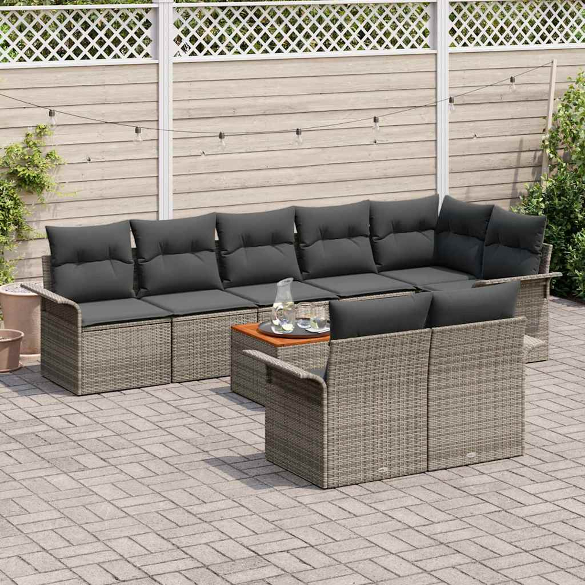 Graues Outdoor-Wickersofa mit dunkelgrauen Kissen. Ein kleiner Tisch mit Gläsern und einer Kanne. Holzzaun und Ziegelterrasse.