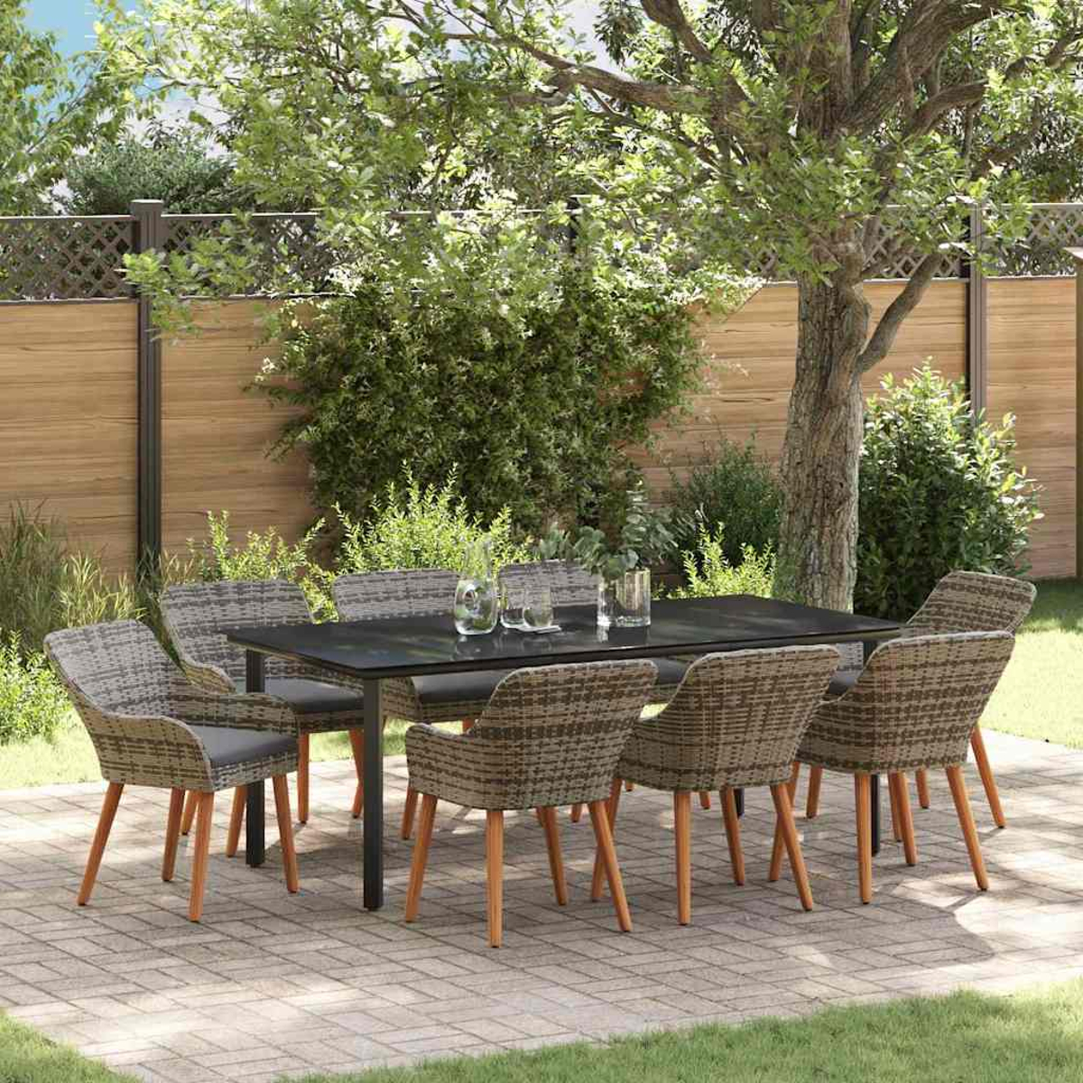Ein Essensemble im Freien mit schwarzem Tisch und gewebten Stühlen steht auf einer Terrasse. Grün und ein Holzzaun sind im Hintergrund.