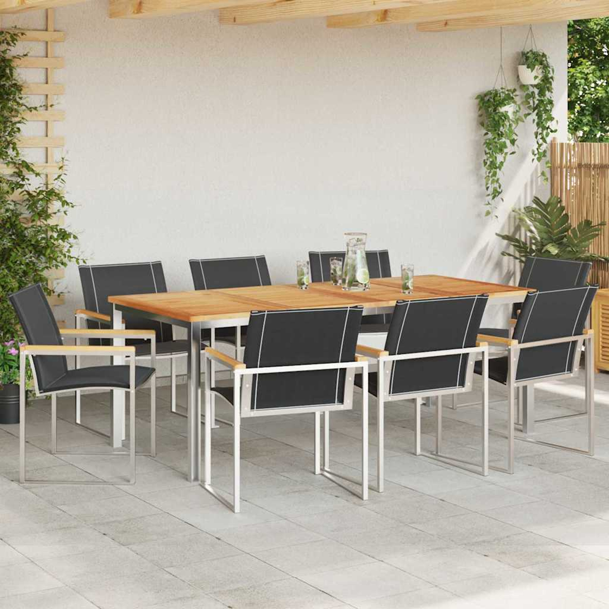 Juego de comedor al aire libre. Mesa de madera con sillas negras. Plantas y una pared blanca en el fondo.