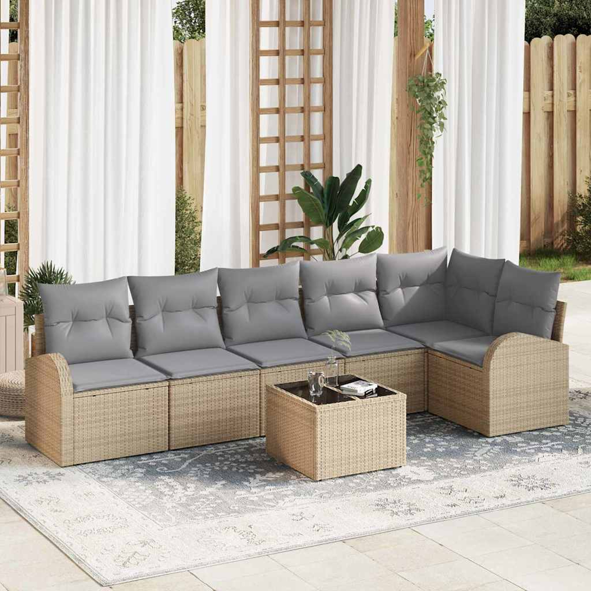 Outdoor-Ecksofa mit grauen Kissen, einem kleinen Tisch und einem gemusterten Teppich. Weiße Vorhänge und Holzzaun im Hintergrund.
