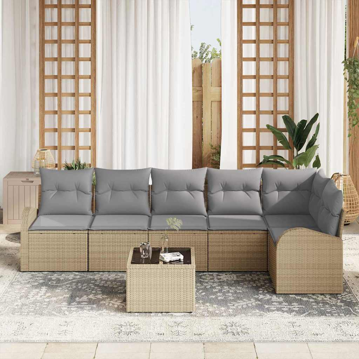 Outdoor-Sitzgruppe mit grauen Kissen, Rattan-Untergestell und einem kleinen Tisch auf einem gemusterten Teppich. Hintergrund ist Vorhänge und Gartenblick.