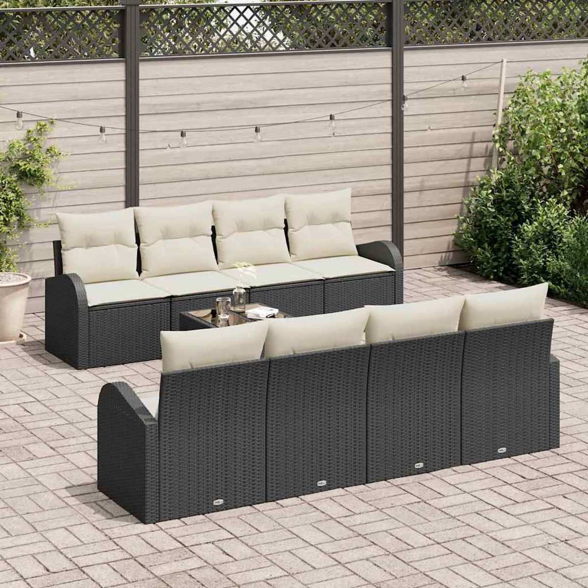 Outdoor-Terrassenset mit schwarzen Korbmöbeln, cremefarbenen Kissen, einem Glastisch und einem Holzzaun im Hintergrund.
