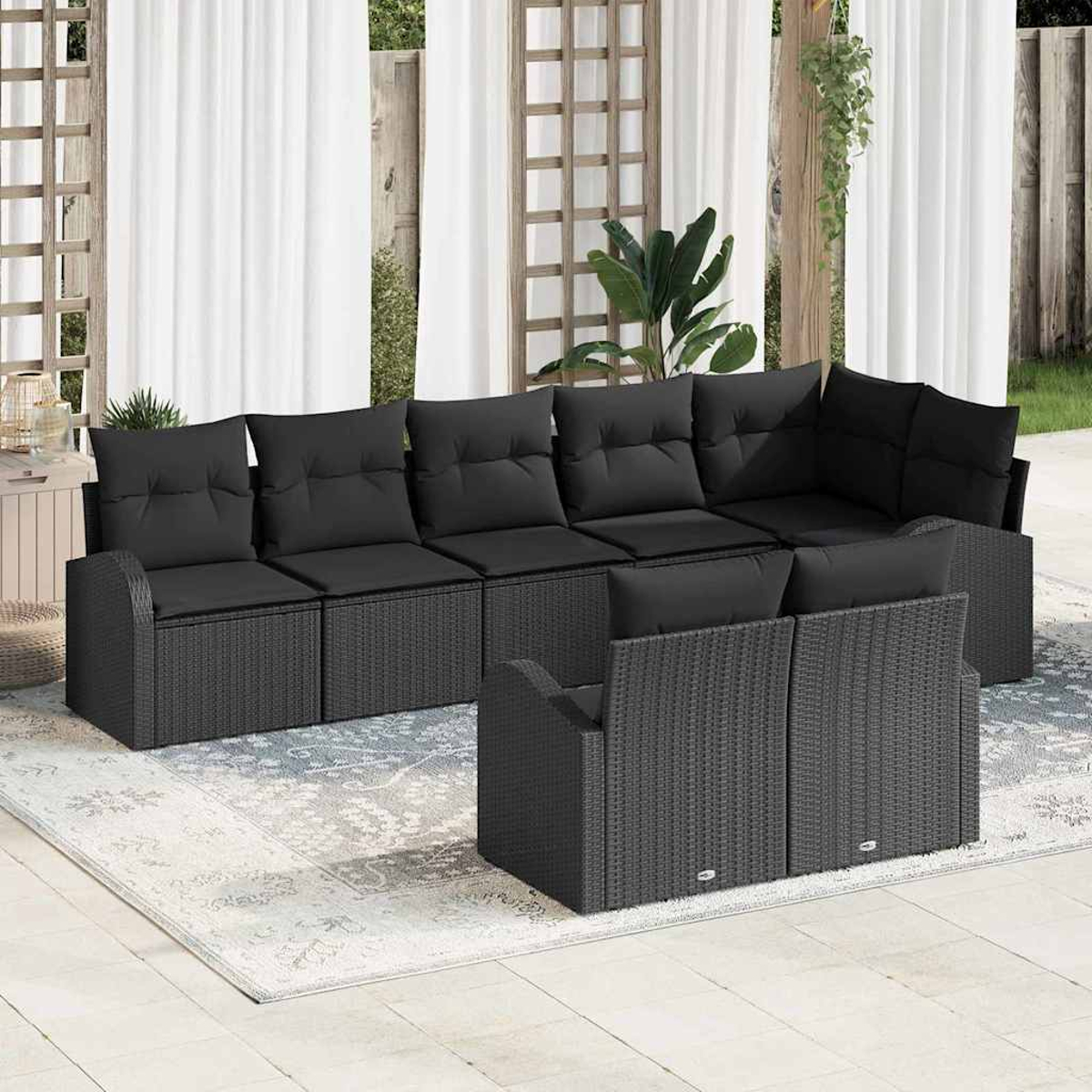 Ein Ecksofa im Freien mit schwarzen Kissen, auf einem gemusterten Teppich. Weiße Vorhänge und Grün im Hintergrund.