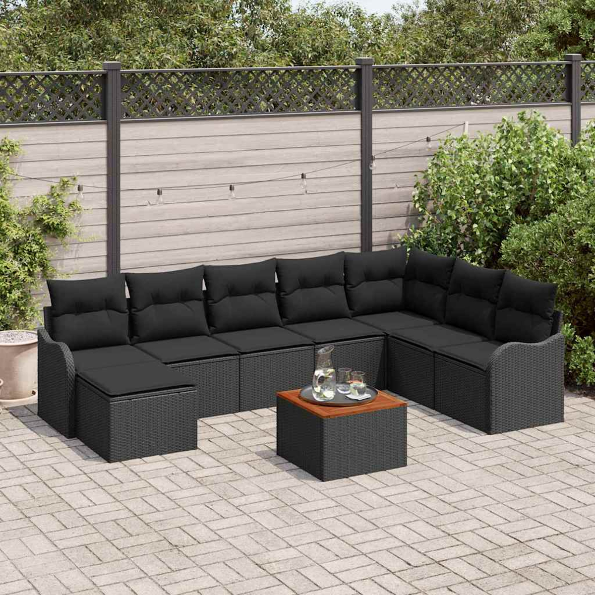 Outdoor-Ecksofa mit schwarzen Kissen, ein kleiner Tisch mit Gläsern und eine Terrasse mit Holzzaun.