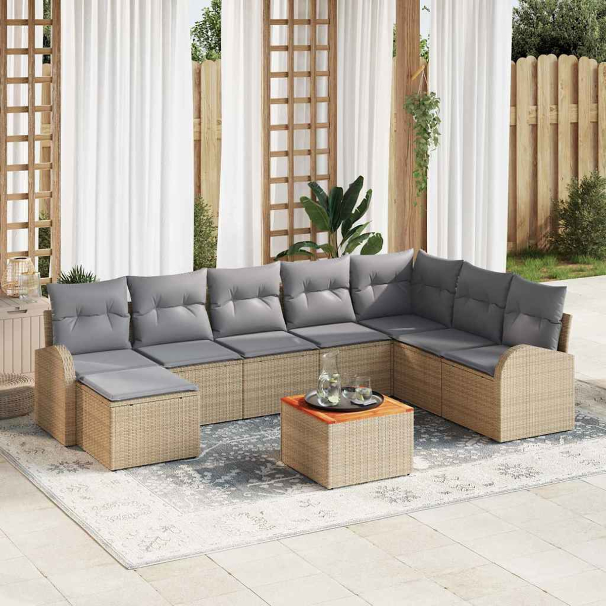 Ein Ecksofa im Freien mit grauen Kissen und einem passenden Couchtisch auf einem gemusterten Teppich, neben weißen Vorhängen.