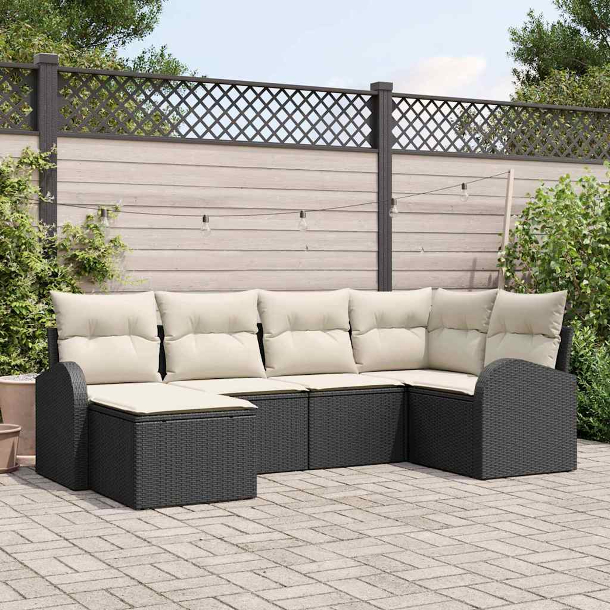 Ein Ecksofa im Freien mit hellen Kissen und dunkelgrauem, gewebtem Rahmen steht auf einer Terrasse. Im Hintergrund sind ein Zaun und Pflanzen zu sehen.