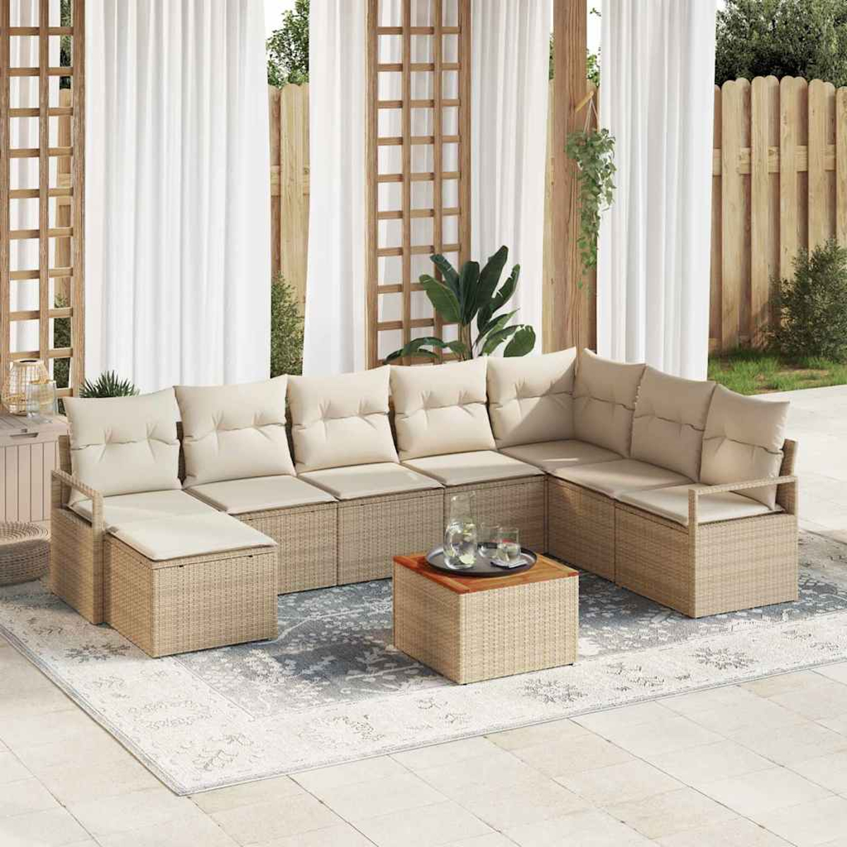 Beiges Outdoor-Ecksofa mit cremefarbenen Kissen steht auf einem gemusterten Teppich. Davor steht ein kleiner Tisch mit Getränken. Weiße Vorhänge und ein Holzzaun sind im Hintergrund.