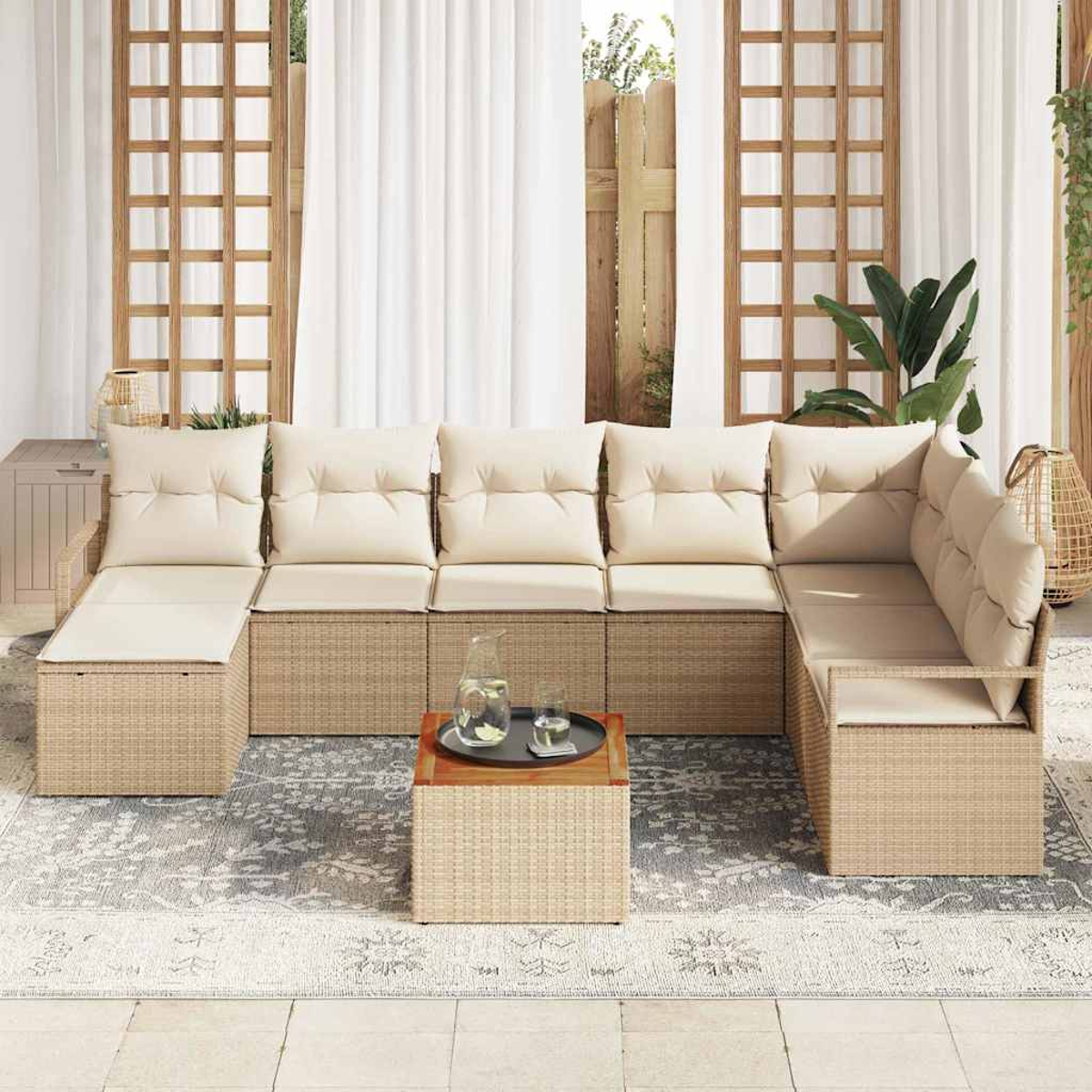 Outdoor-Wicker-Ecksofa mit cremefarbenen Kissen. Ein kleiner Tisch mit Tablett, Kanne und Glas. Weiße Vorhänge und ein gemusterter Teppich.