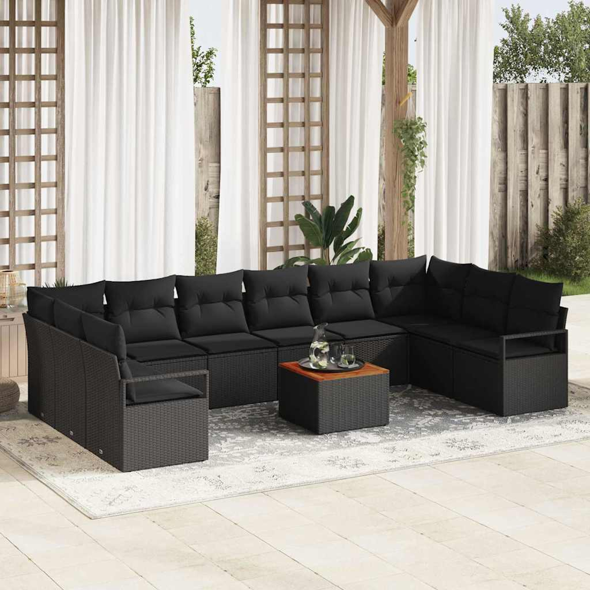 Außensitzbereich mit schwarzem Ecksofa, Holztisch und weißen Vorhängen. Hintergrund zeigt einen Holzzaun.