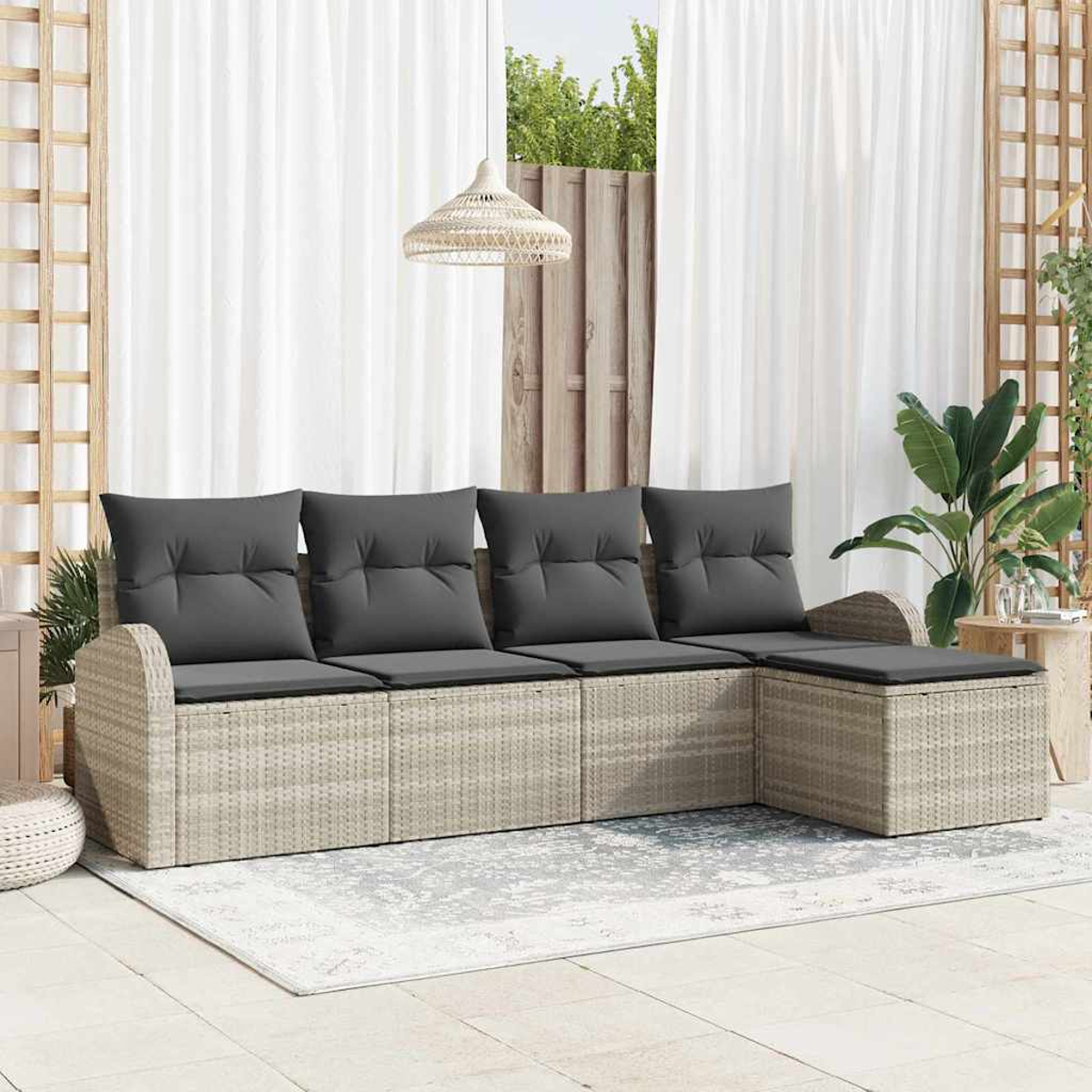 Wicker-Sofa im Freien mit grauen Kissen. Weiße Vorhänge, eine Hängeleuchte und Pflanzen schaffen eine entspannte Atmosphäre. Ein Teppich und Holzgitter sind zu sehen.