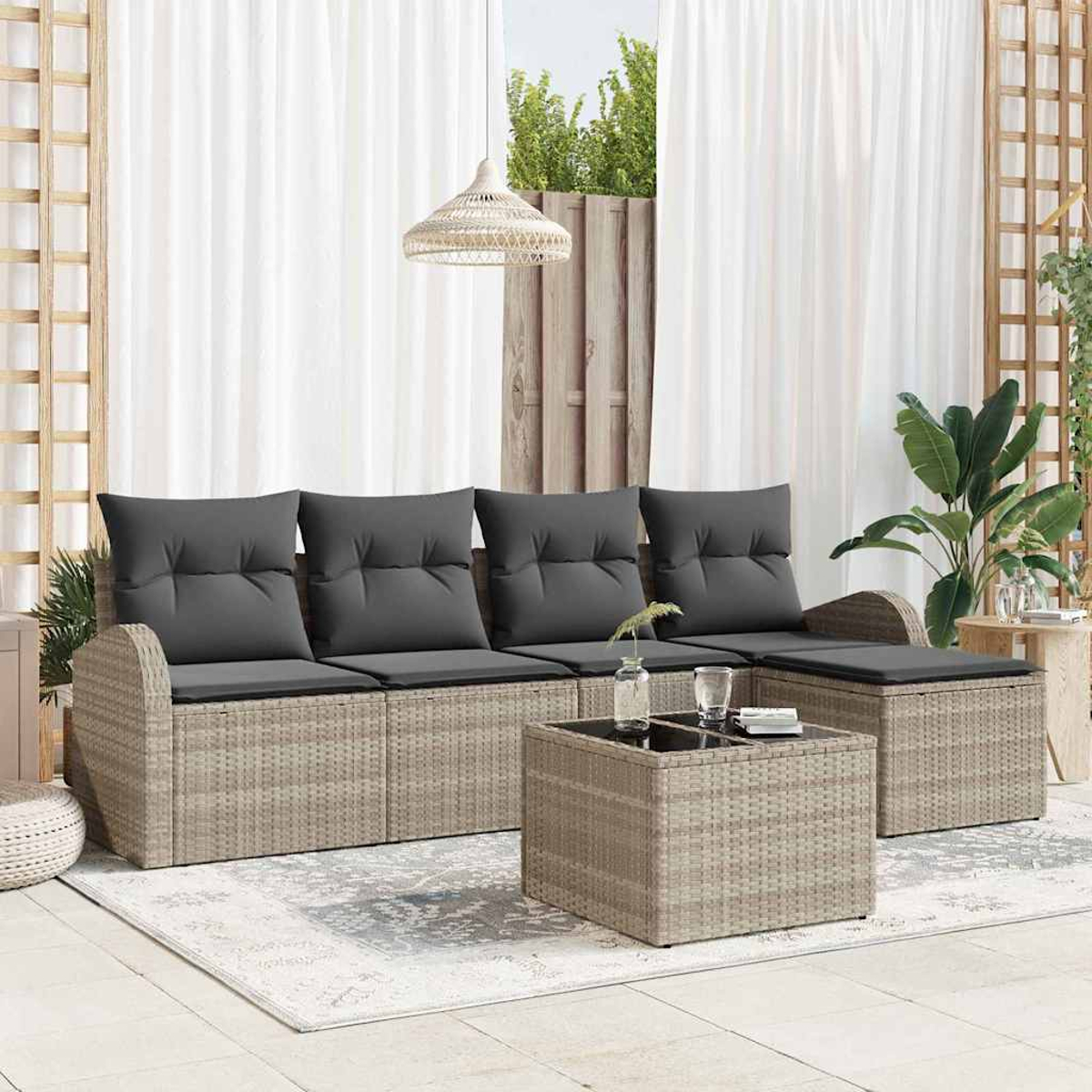 Garten-Sitzgruppe mit grauen Kissen, Rattangestell und Couchtisch auf einem Teppich, in der Nähe weißer Vorhänge und Pflanzen.