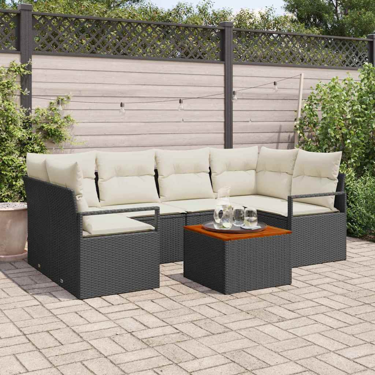 Outdoor-Ecksofa mit cremefarbenen Kissen und einem Couchtisch mit Getränken. Auf einer Steinterrasse mit Holzzaun im Hintergrund.