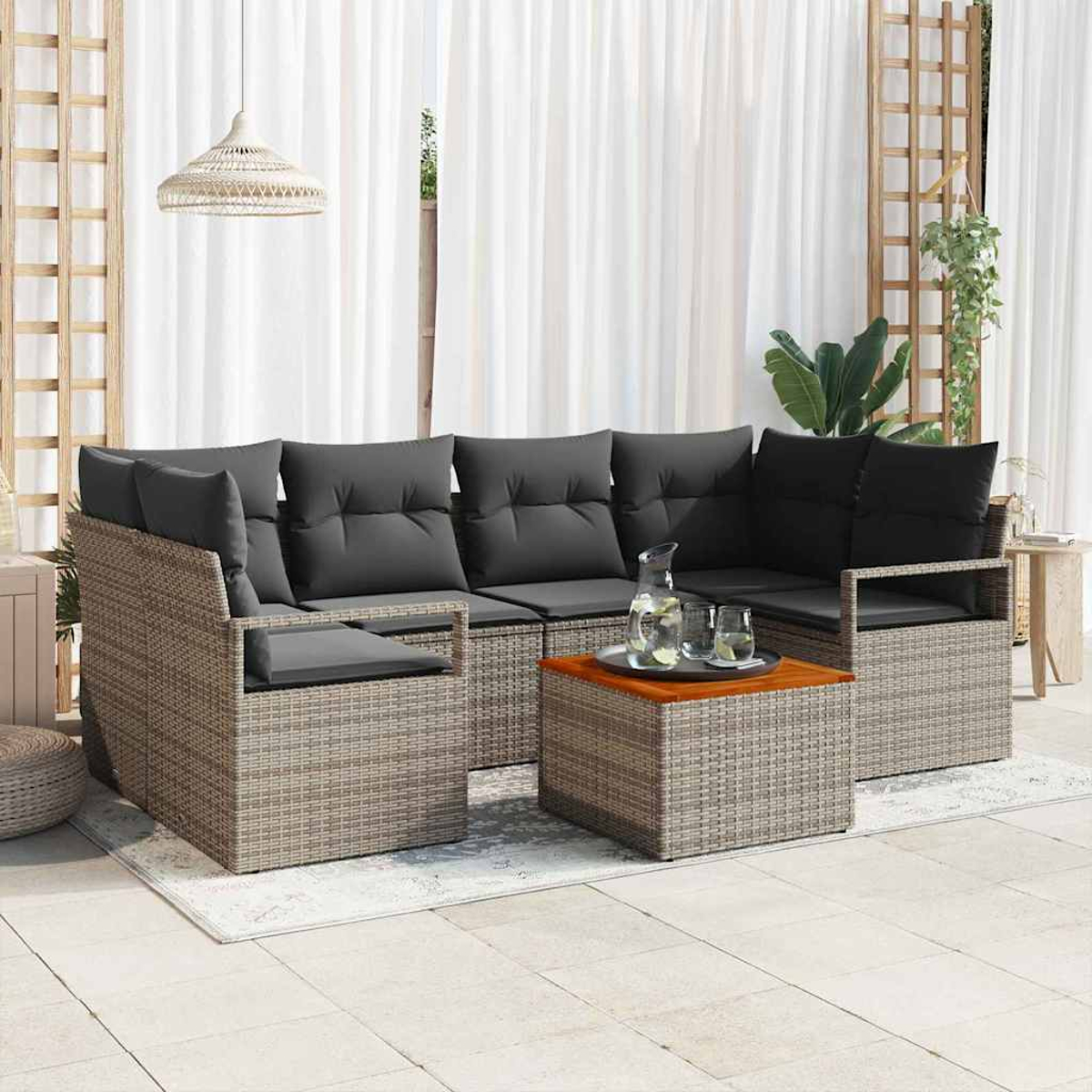 Wicker-Außensofa mit grauen Kissen und einem hölzernen Couchtisch. Weiße Vorhänge und dekorative Pflanzen im Hintergrund.