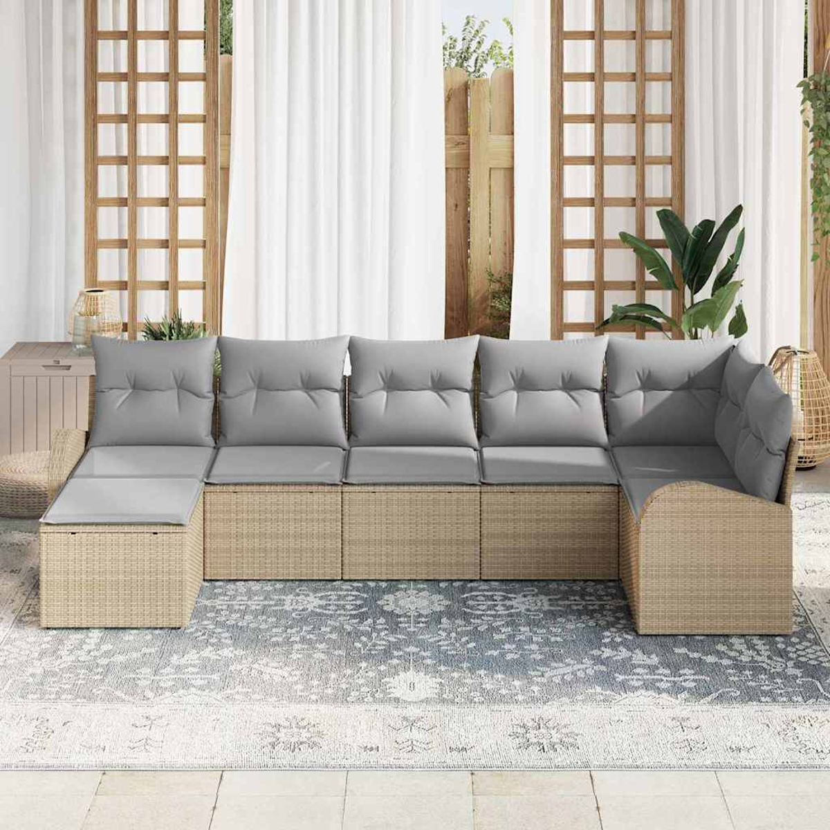 Ein beiges Ecksofa mit grauen Kissen steht auf einem gemusterten Teppich. Dahinter ein Fenster mit weißen Vorhängen und Holzrahmen.