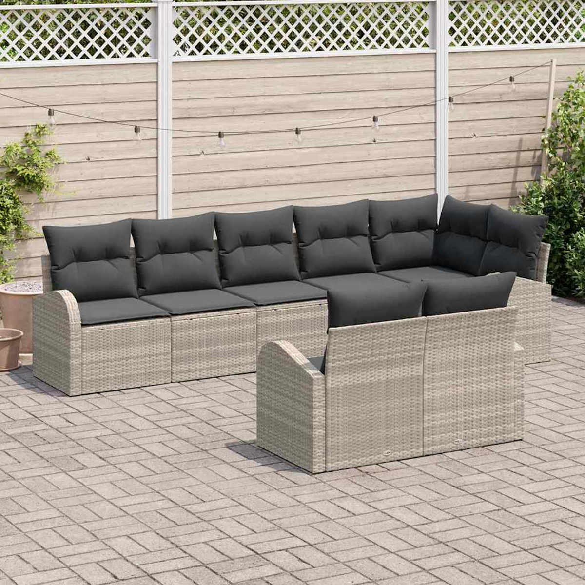 Outdoor-Ecksofa mit grauen Kissen auf einer Backstein-Terrasse. Dahinter ein Holzzaun mit weißem Gitter und Lichterketten.
