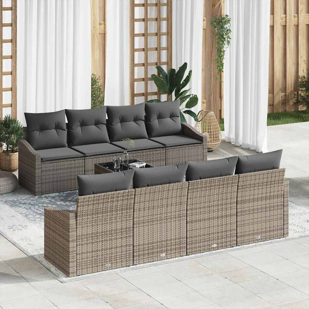 Juego de patio al aire libre con cojines grises. Dos sofás de mimbre y una mesa pequeña están en un patio con cortinas blancas y valla de madera.