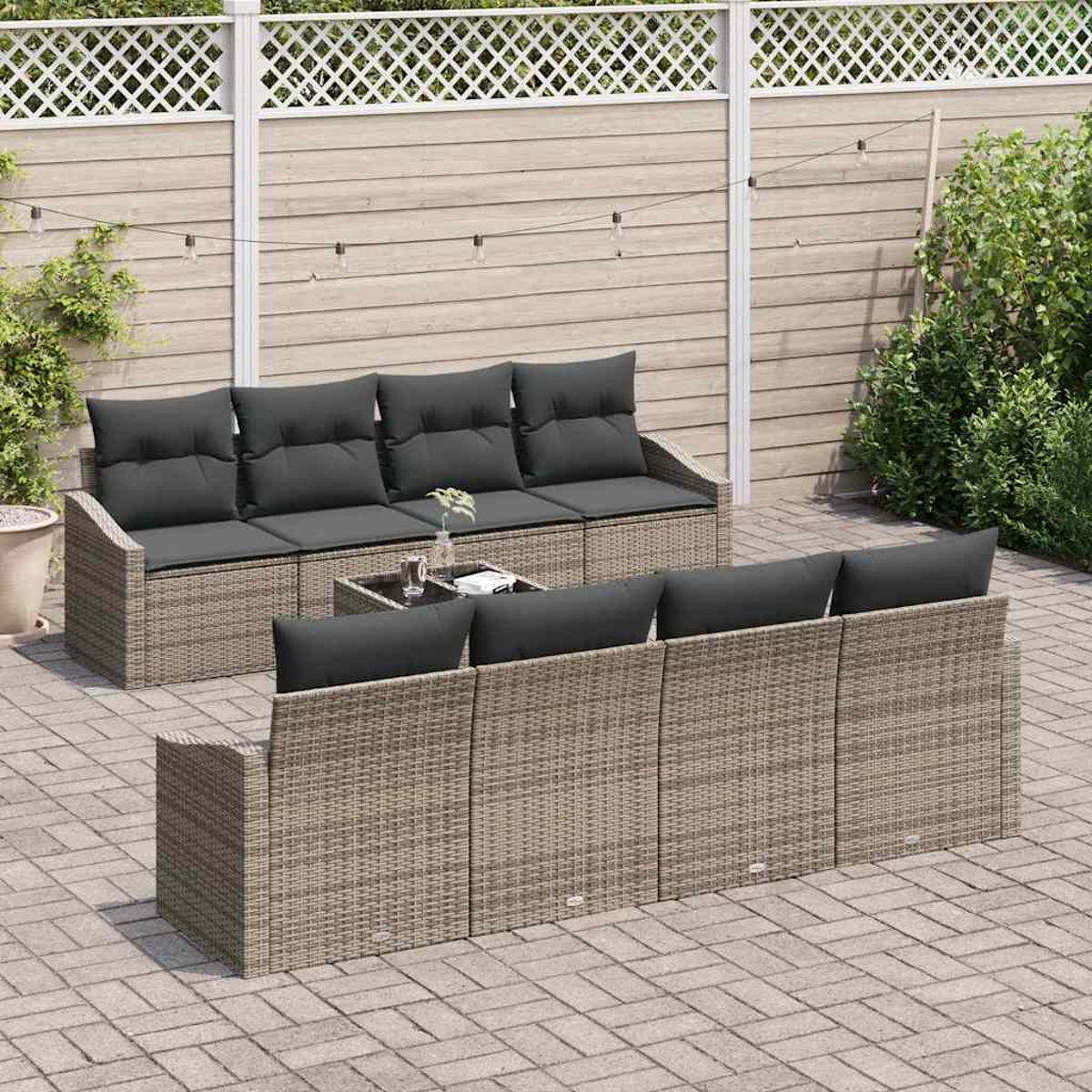 Conjunto de muebles de ratán para exterior con cojines grises. Una mesa de centro con plantas está frente a los sofás, en un patio.