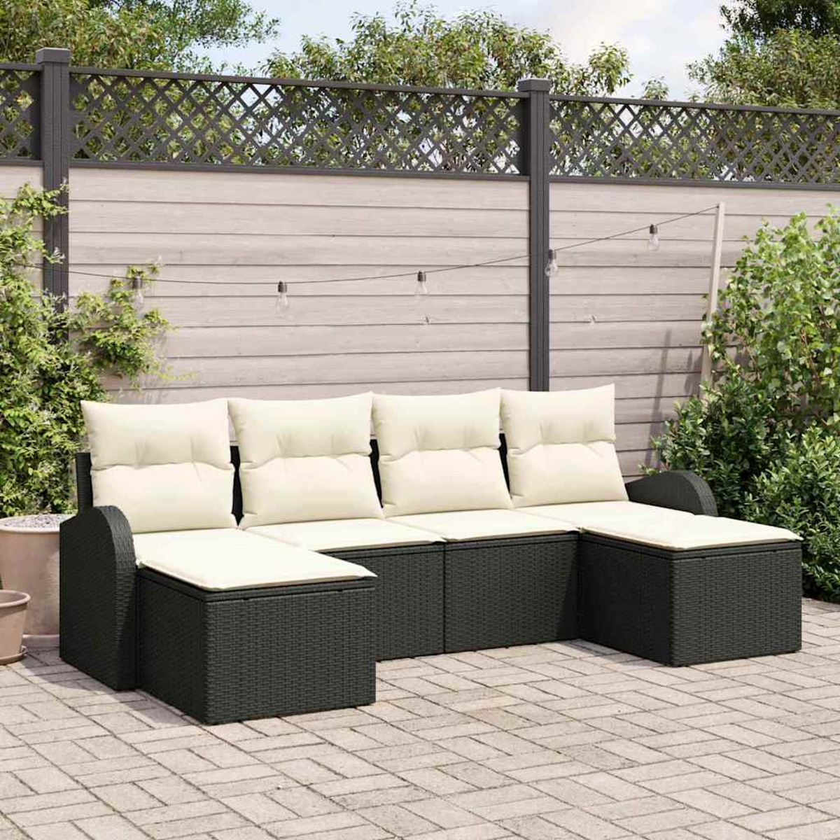 Outdoor-Ecksofa mit beigefarbenen Kissen und grauem Korbgeflecht. Auf einer Terrasse mit Holzzaun und Grün im Hintergrund.