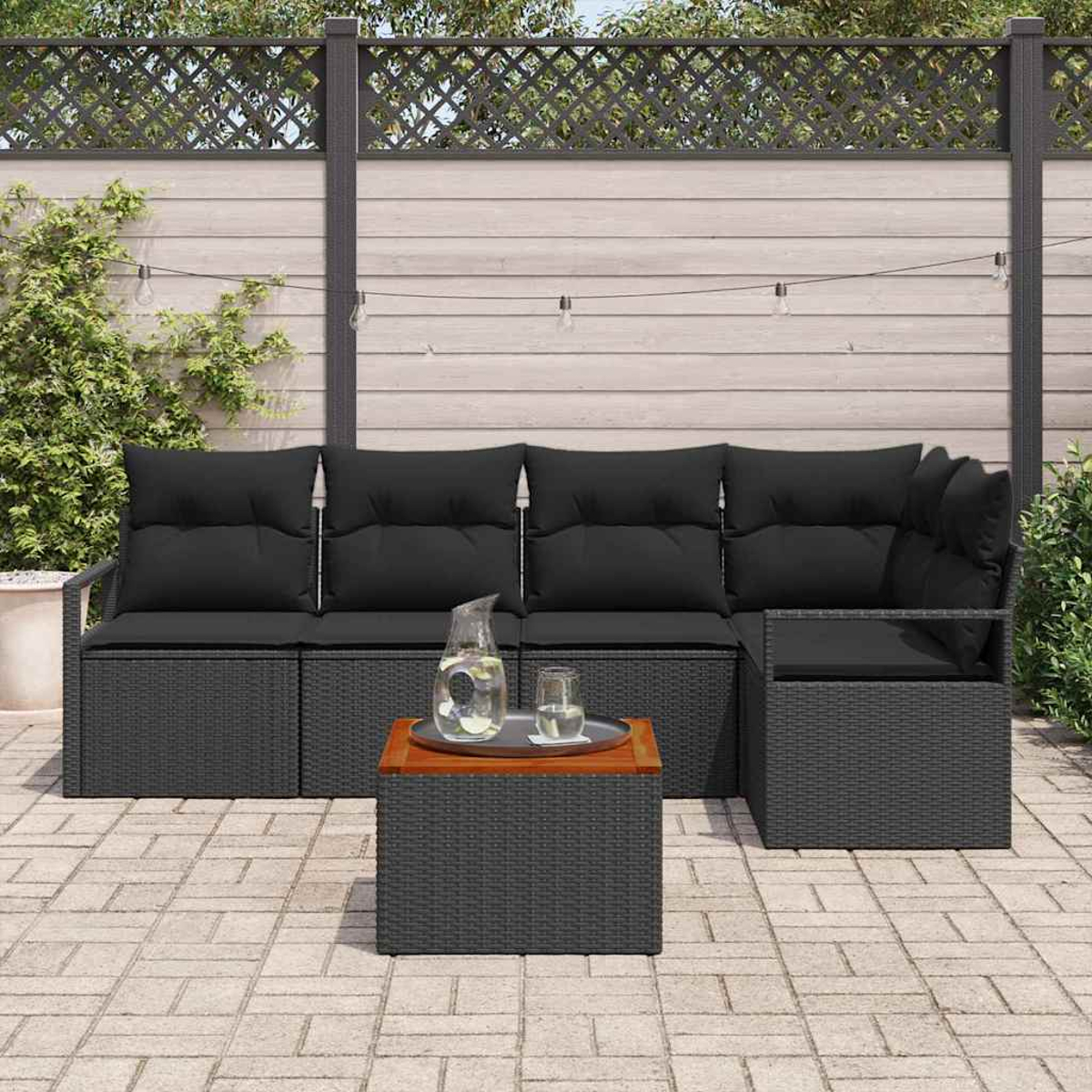 Outdoor-Ecksofa mit schwarzen Kissen, kleinem Tisch mit Getränken und Holzzaun im Hintergrund.