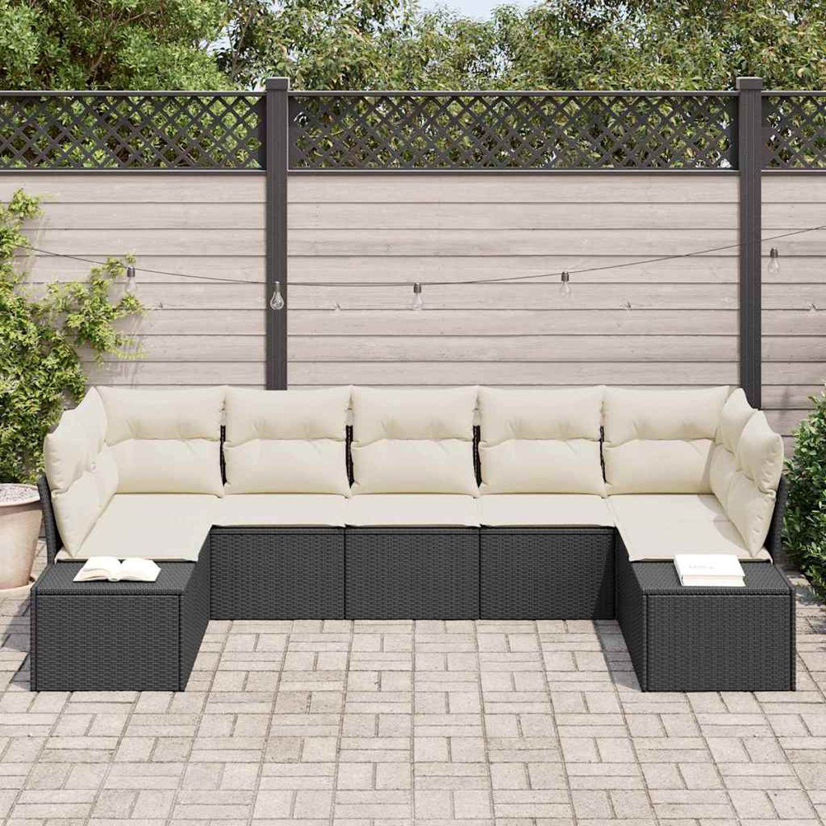 Ein U-förmiges Outdoor-Sofa mit cremefarbenen Kissen und schwarzem Korbgewebe. Bücher liegen auf den Beistelltischen. Ein Zaun und Grünzeug sind im Hintergrund.