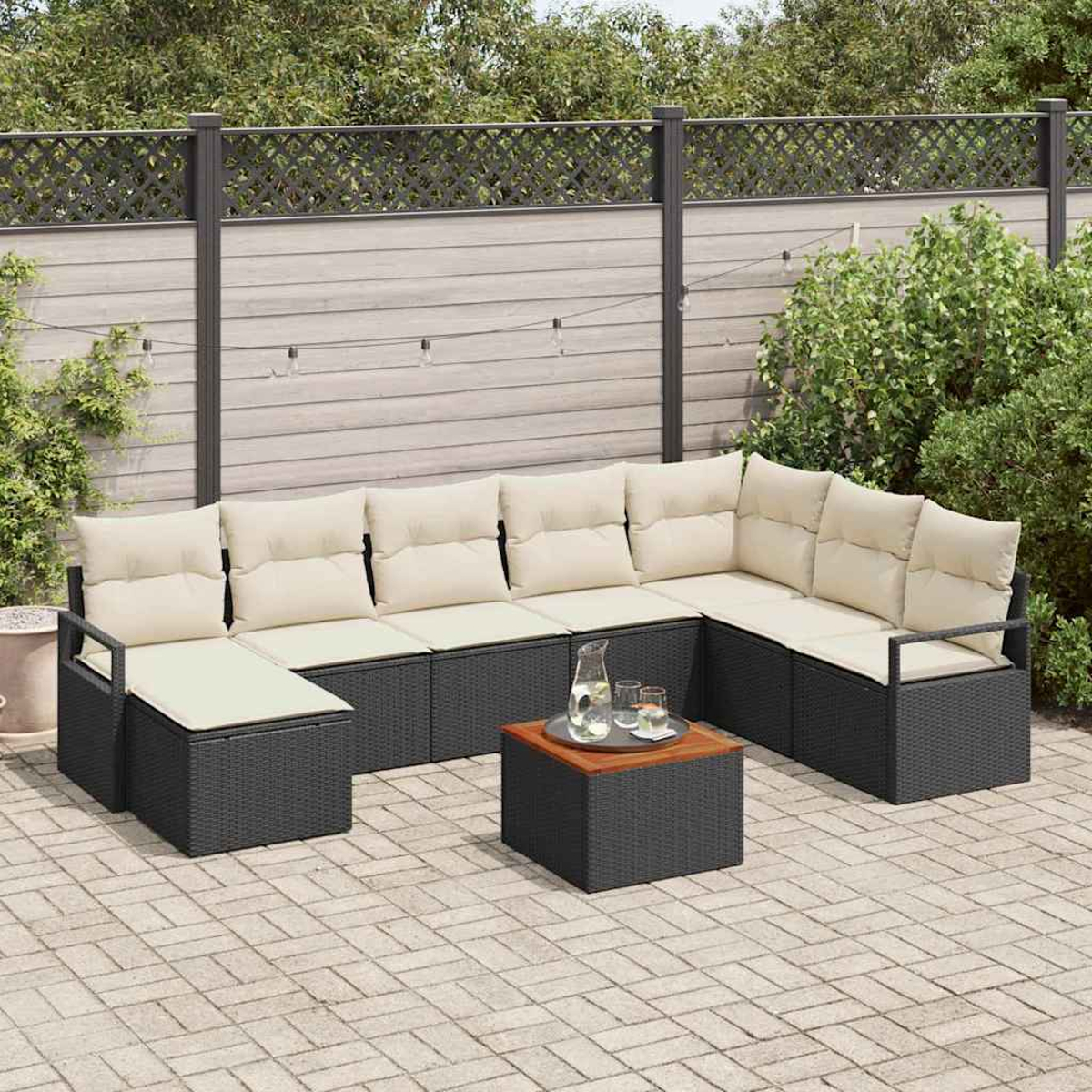 Outdoor-Ecksofa mit beigen Kissen. Ein kleiner Tisch mit Getränken steht davor. Zaun und Grün im Hintergrund.
